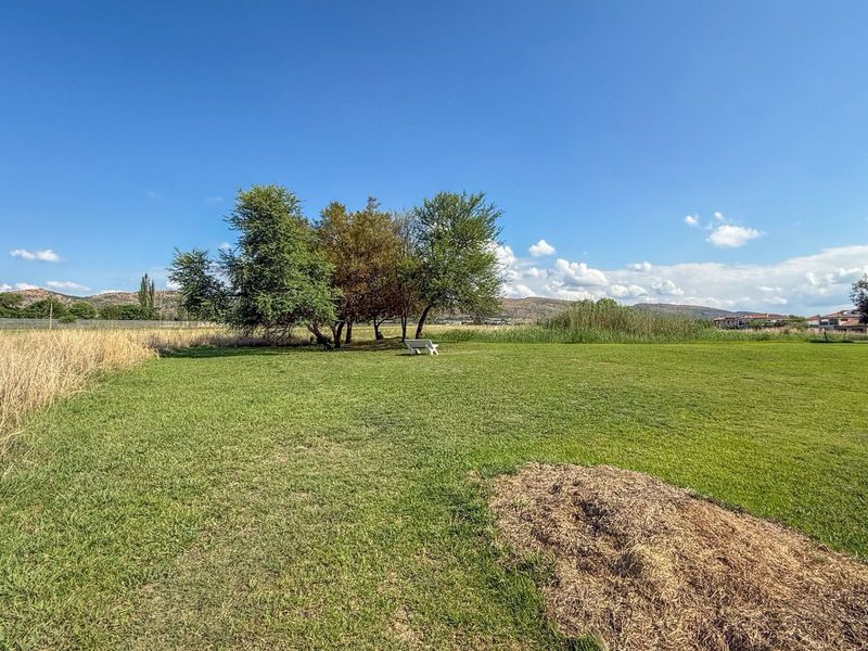 A spacious, well-maintained grassy plot featuring mature trees and scenic landscape views, ideal for residential development.
