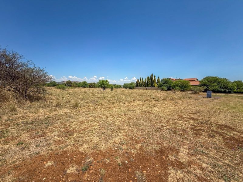 A wide-angle view of a vacant residential plot featuring natural vegetation and an electrical utility connection point.