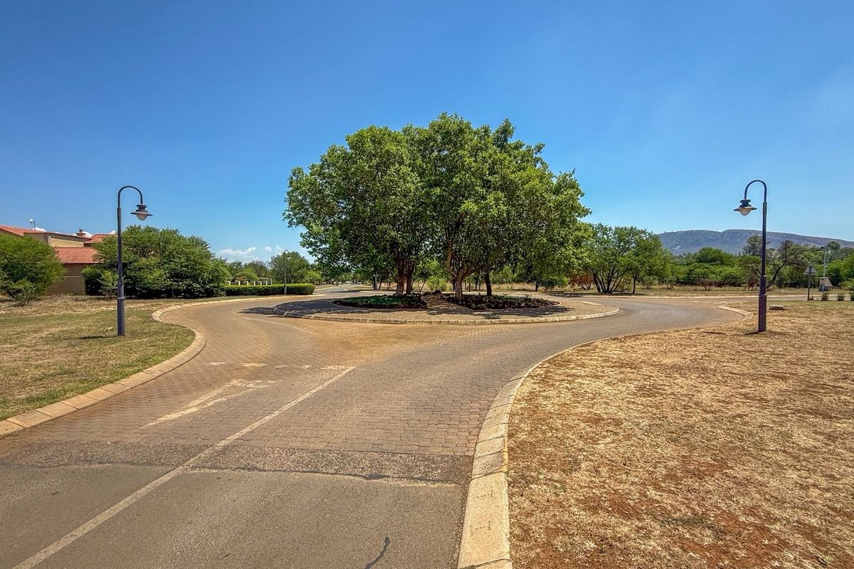 A view of a paved residential roundabout featuring a landscaped central island with mature trees and street lighting in a well-maintained estate setting.