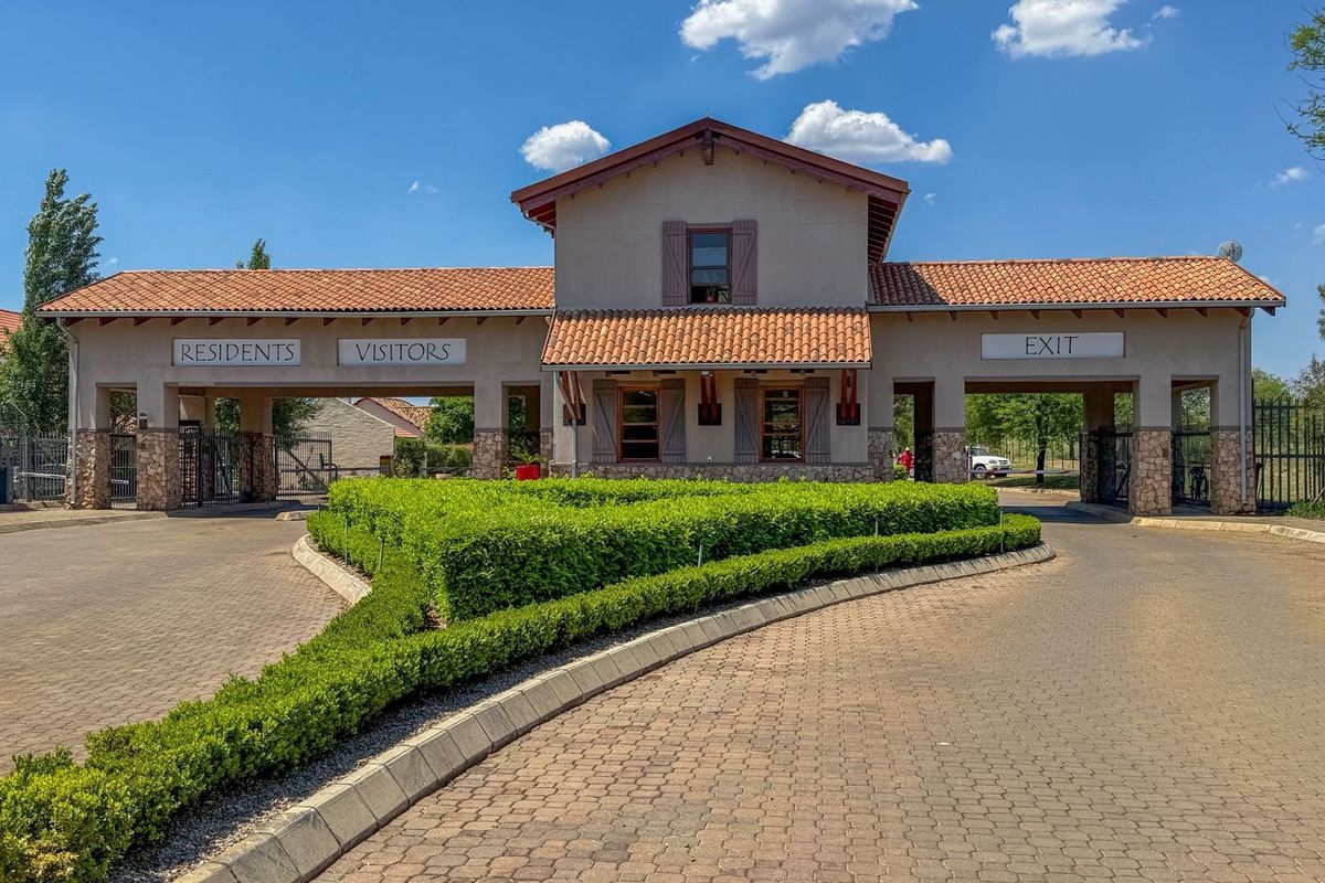 A well-maintained residential estate security gatehouse featuring stone cladding, tiled roofing, and separate access lanes for residents and visitors.