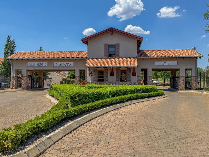 A well-maintained residential estate security gatehouse featuring stone cladding, tiled roofing, and separate access lanes for residents and visitors.