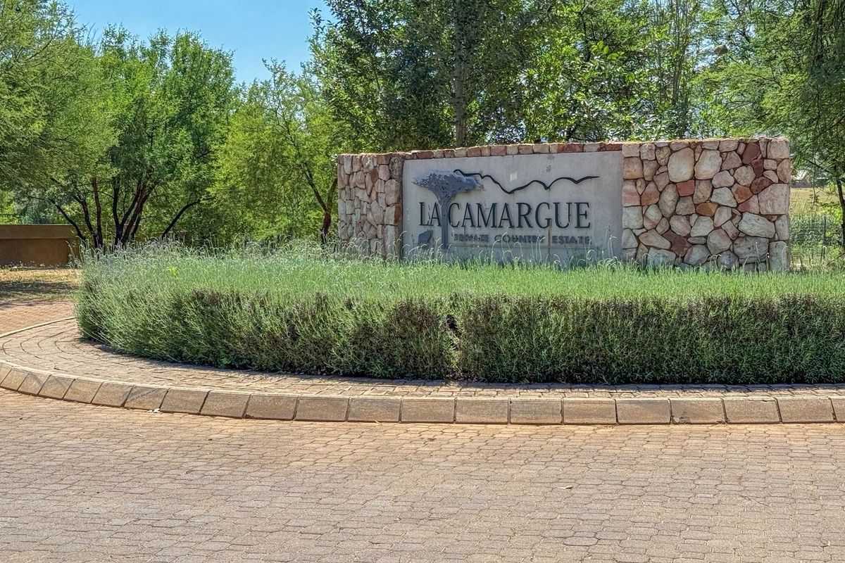The entrance to La Camargue Private Country Estate featuring a stone masonry wall, paved roundabout, and well-maintained landscaping.