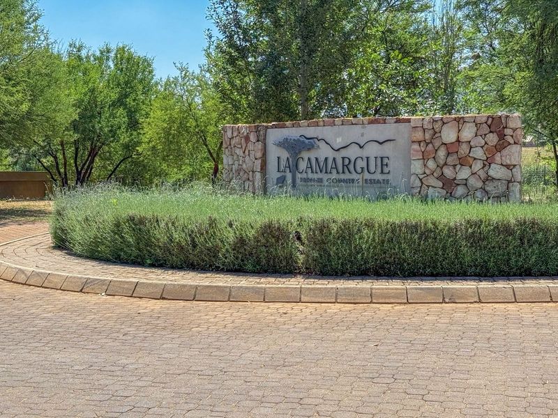 The entrance to La Camargue Private Country Estate featuring a stone masonry wall, paved roundabout, and well-maintained landscaping.