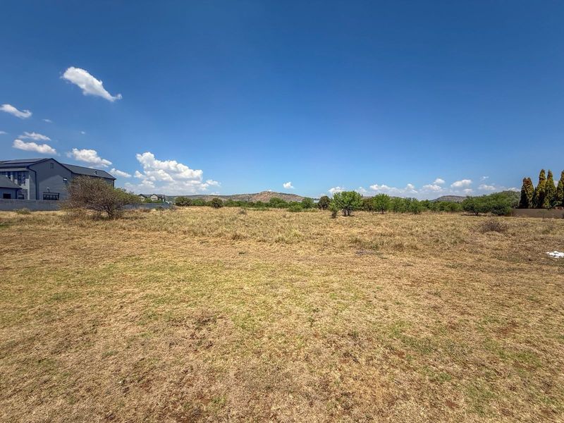 A wide-angle view of a vacant residential plot featuring natural grass cover and distant mountain views.