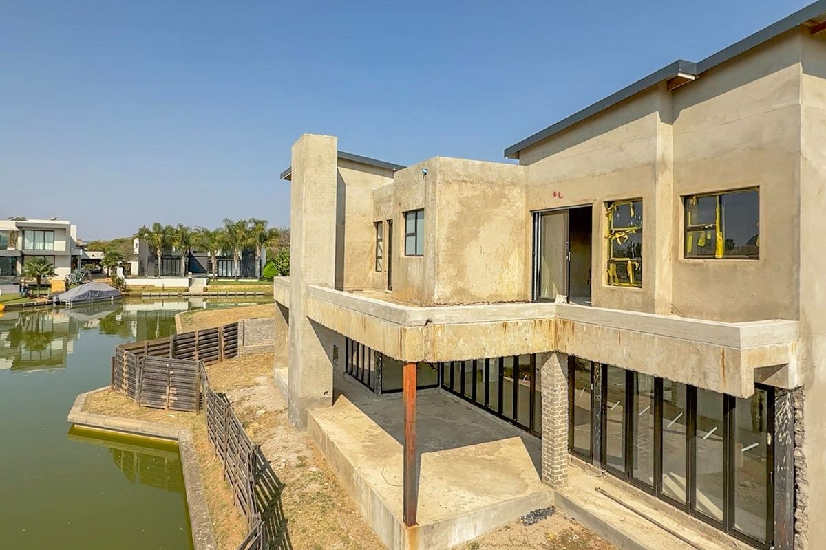 Rear view of a waterfront property under construction, featuring large aluminium sliding doors, an expansive concrete balcony, and unfinished exterior plaster walls.