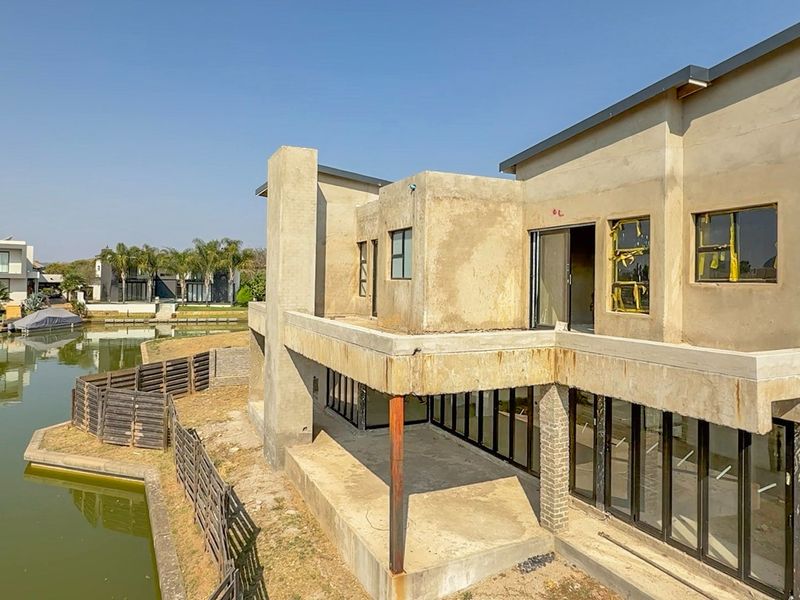 Rear view of a waterfront property under construction, featuring large aluminium sliding doors, an expansive concrete balcony, and unfinished exterior plaster walls.