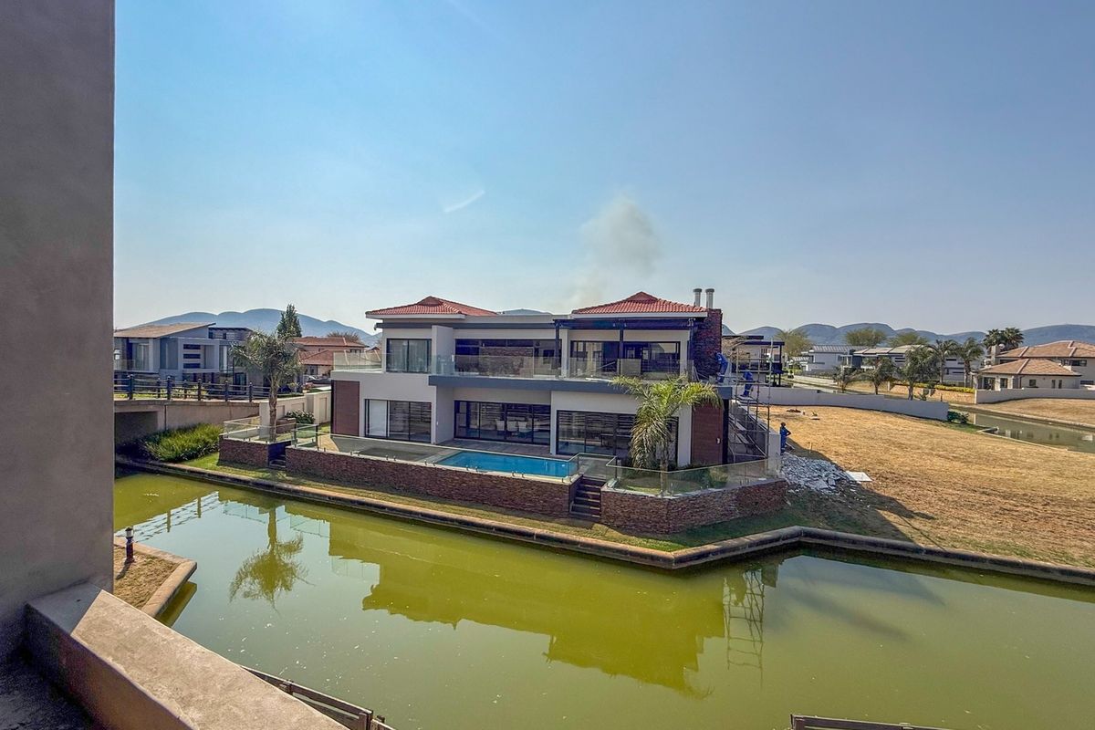 Aerial view of a modern two-story waterfront residence featuring a private swimming pool, glass balustrades, and stone cladding, situated along a canal.
