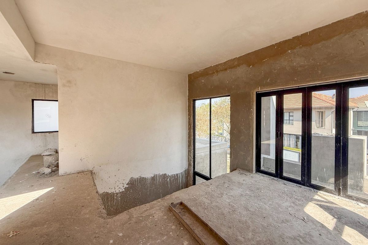An unfinished interior space featuring black aluminium framed windows and doors, currently in a shell condition awaiting final flooring and wall finishes.