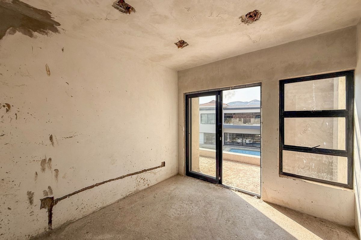 An unfinished bedroom interior featuring exposed plaster walls, ceiling electrical points, and aluminium sliding doors leading to an outdoor area.