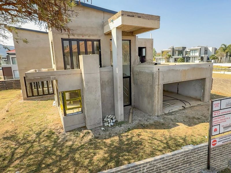 A modern residential property under construction, featuring a double garage, concrete facade, and balcony, currently in the shell stage of development.