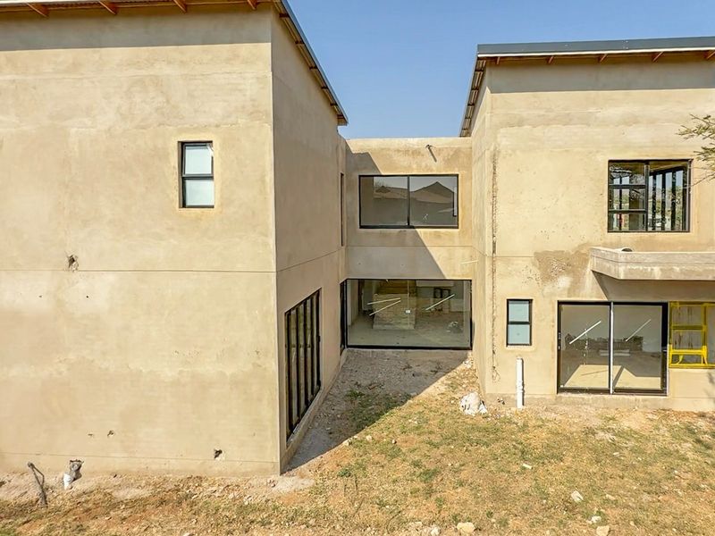 Rear view of a double-story residential property under construction, featuring plastered walls, modern aluminium window frames, and large sliding glass doors.
