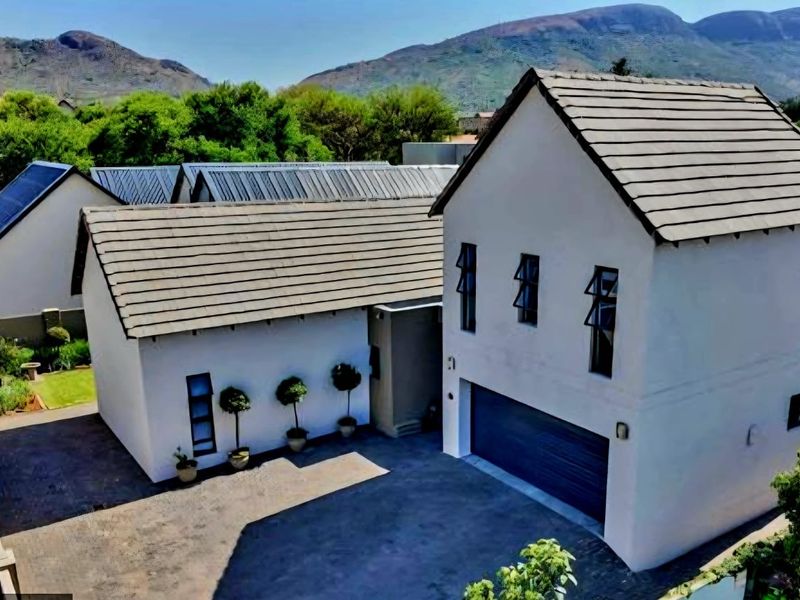 Aerial view of a modern residential property featuring a double garage, tiled roof, and paved driveway set against a scenic mountain backdrop.