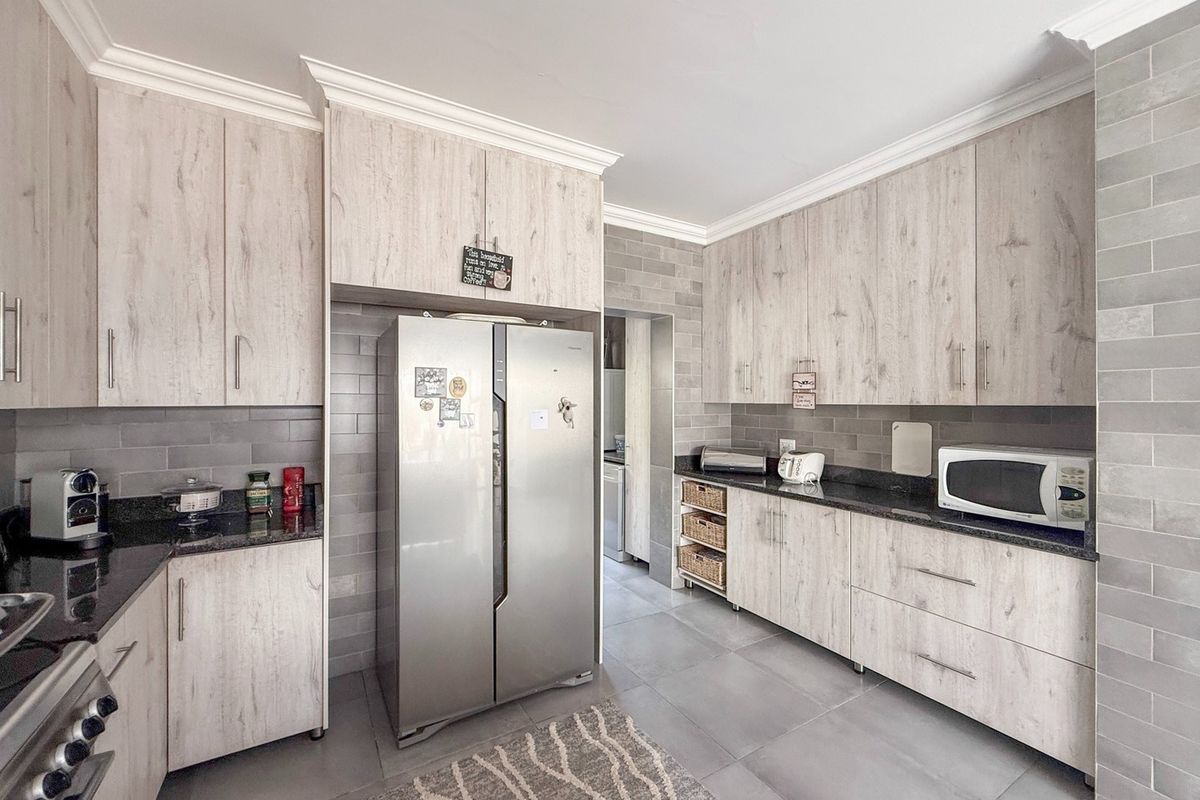 Modern kitchen featuring light wood-grain cabinetry, dark granite countertops, subway tile backsplash, and integrated appliances with a clean, contemporary aesthetic.