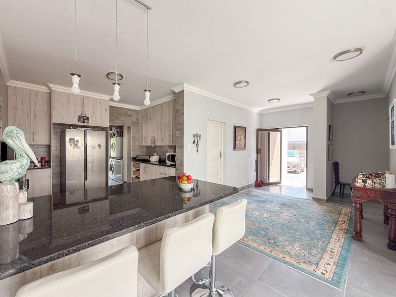 Spacious open-plan kitchen and living area featuring a large granite island, modern cabinetry, and neutral tiled flooring with direct access to the exterior.