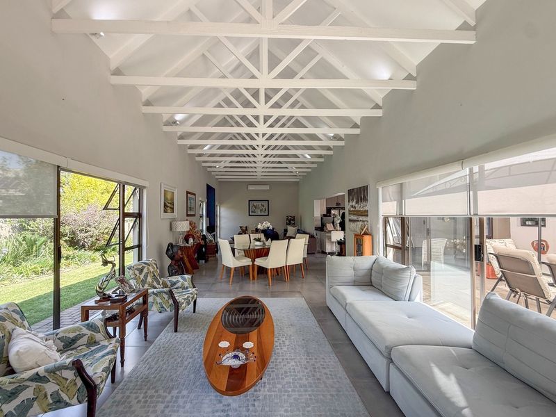 Spacious open-plan living and dining area featuring high vaulted ceilings with exposed white timber trusses, tiled floors, and large sliding doors opening to the garden.