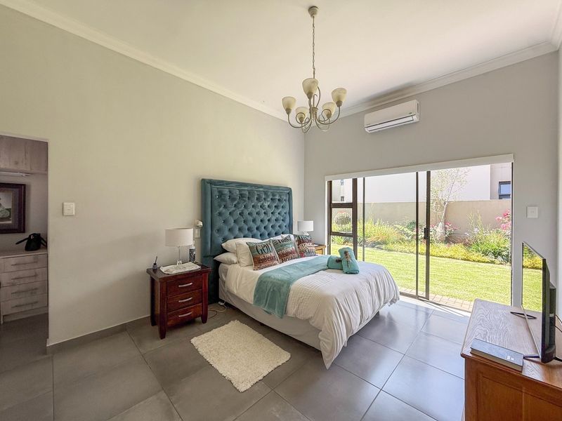 Spacious bedroom featuring large sliding glass doors opening to a private garden, tiled flooring, air conditioning, and elegant ceiling lighting.
