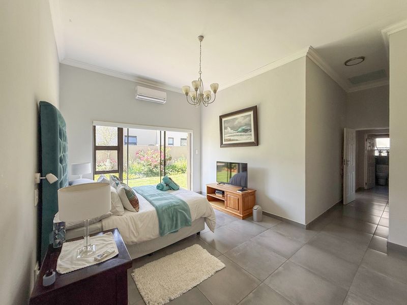 A well-maintained bedroom featuring large sliding glass doors with garden views, neutral tiled flooring, and a split-system air conditioning unit.
