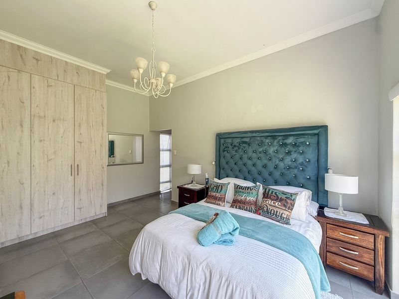 A well-maintained bedroom featuring neutral tiled flooring, built-in wood-grain cupboards, and a decorative chandelier, offering a clean and functional living space.