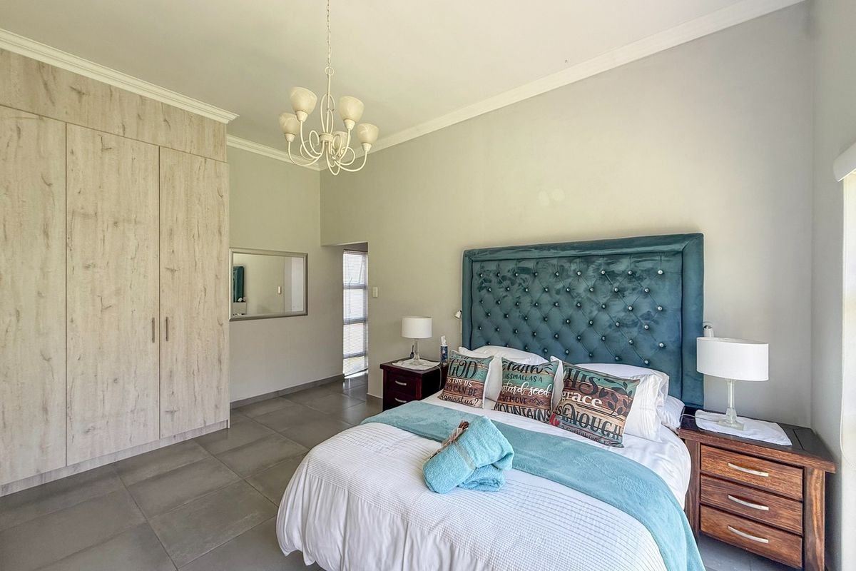 A well-maintained bedroom featuring neutral tiled flooring, built-in wood-grain cupboards, and a decorative chandelier, offering a clean and functional living space.