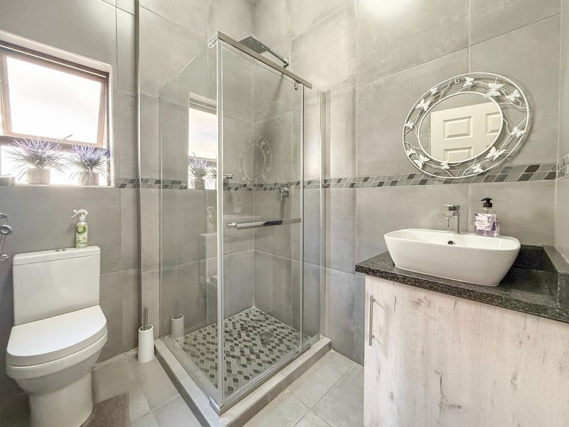 Modern bathroom featuring a glass-enclosed shower, vessel sink on a granite vanity, and neutral grey floor-to-ceiling tiling.