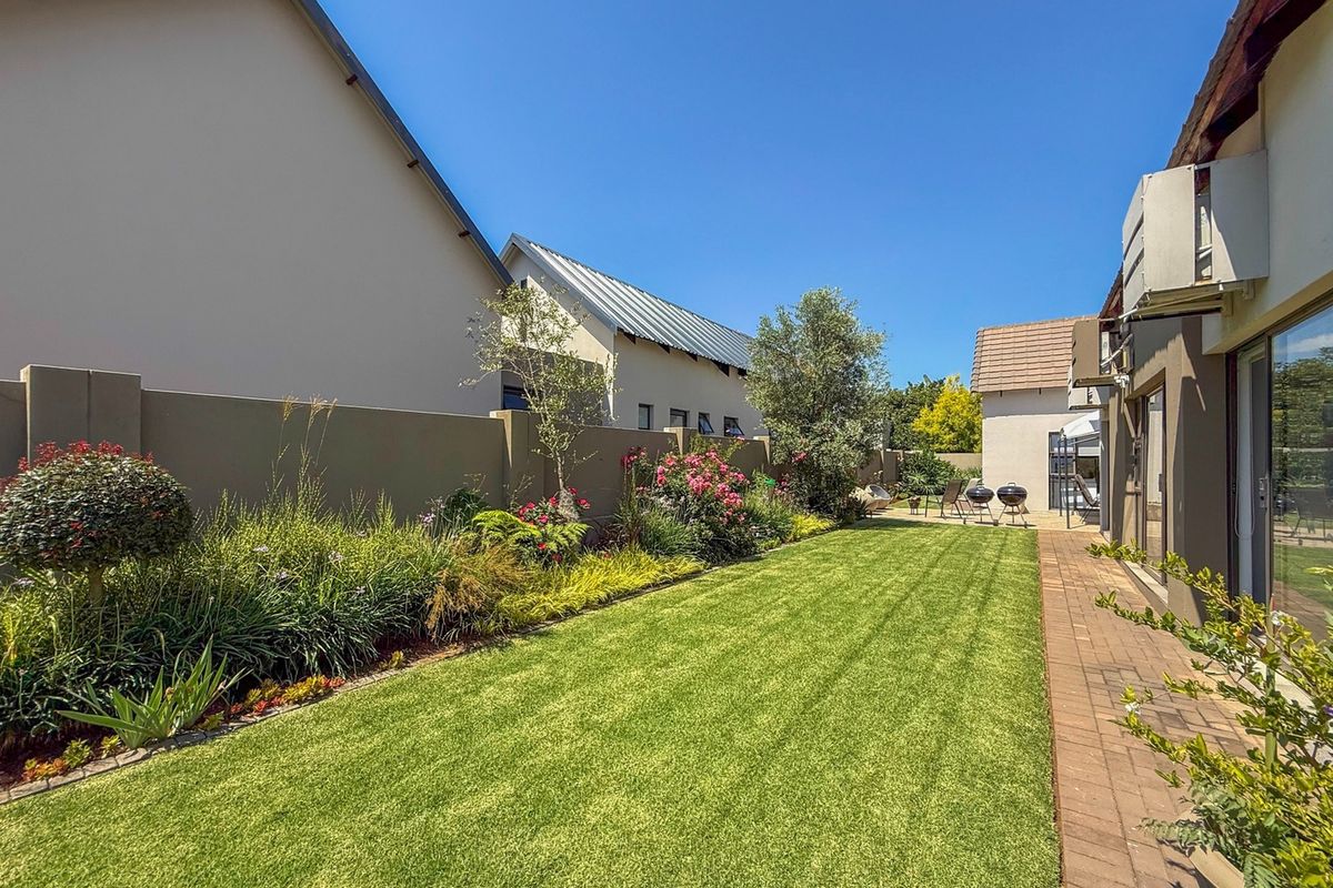 A well-maintained rear garden featuring a manicured lawn, paved walkway, and established garden beds enclosed by a solid boundary wall.