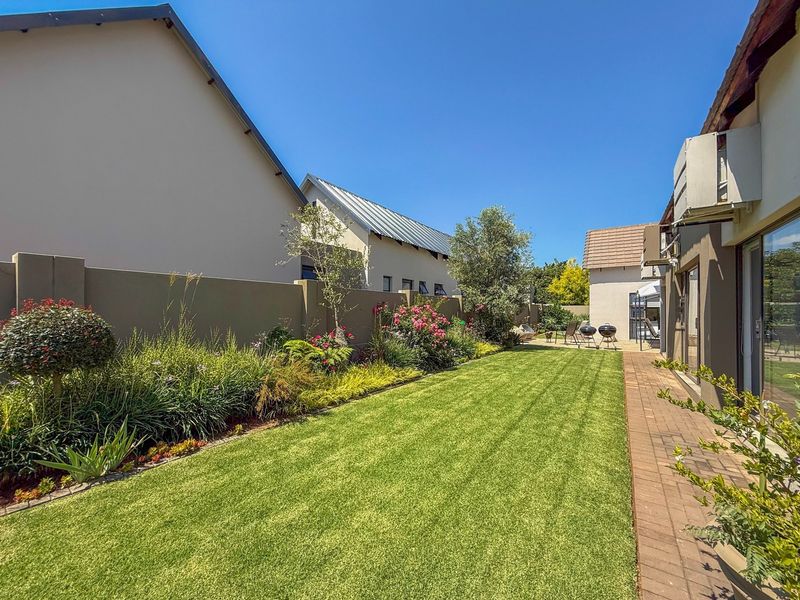 A well-maintained rear garden featuring a manicured lawn, paved walkway, and established garden beds enclosed by a solid boundary wall.