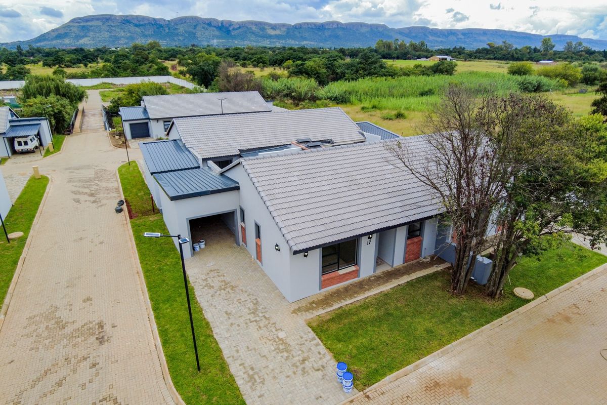 Aerial view of a modern retirement village unit featuring a tiled roof, paved driveway, and garage, set within a landscaped estate with mountain views.