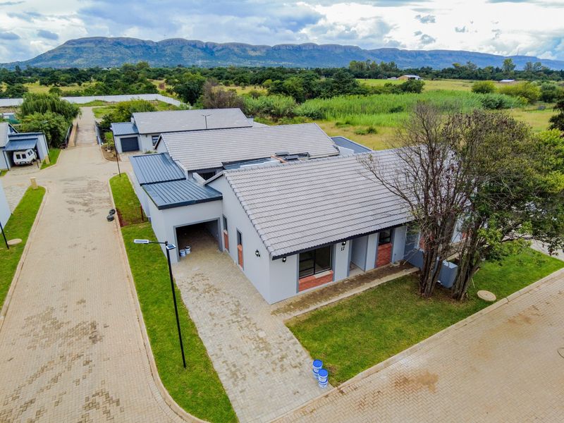Aerial view of a modern retirement village unit featuring a tiled roof, paved driveway, and garage, set within a landscaped estate with mountain views.