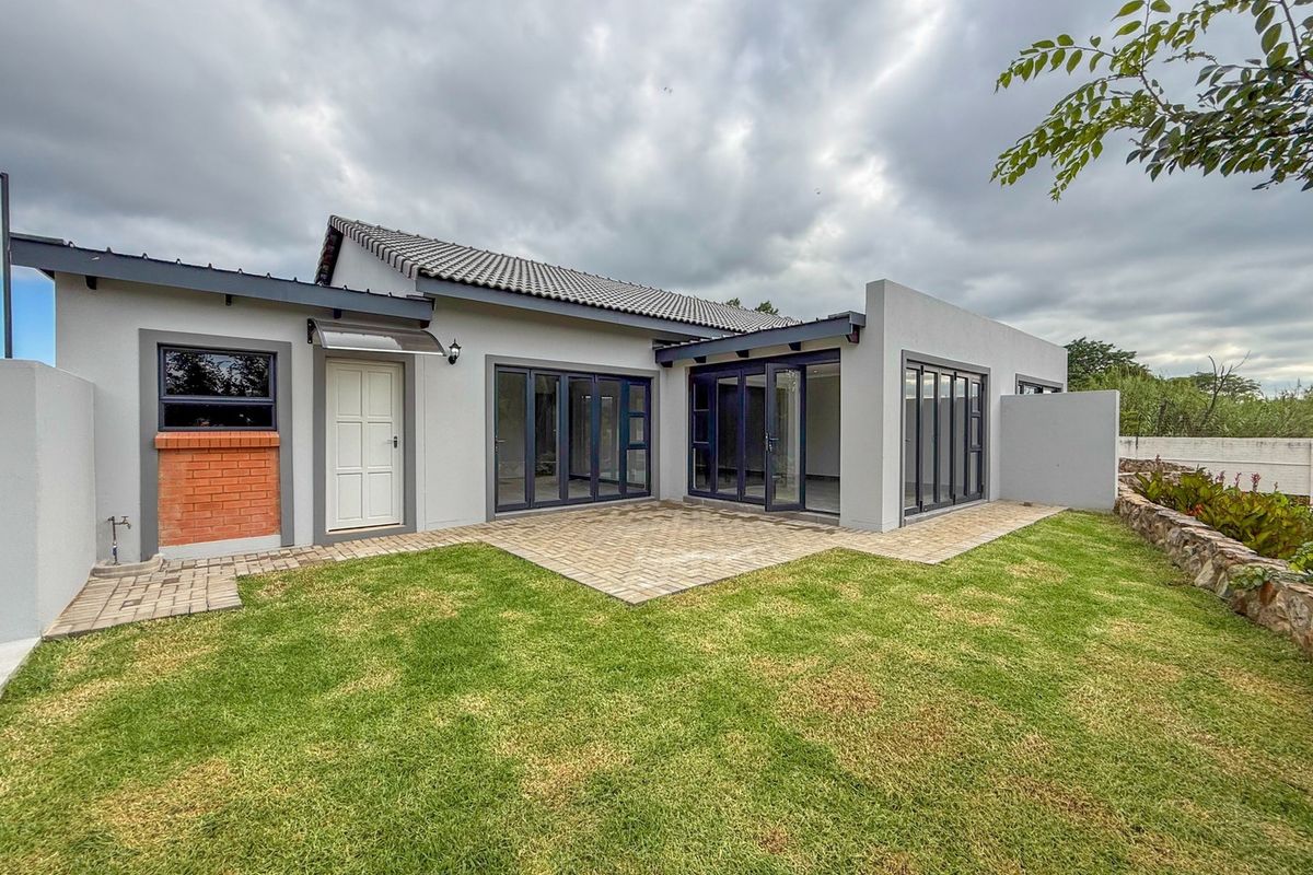 Rear view of a modern retirement unit featuring a paved patio, large aluminium stacker doors, and a well-maintained private garden area.