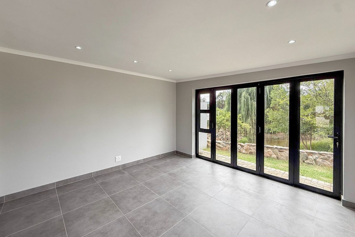 A bright, empty living room featuring modern grey floor tiles, recessed downlights, and black aluminium bifold doors opening to a garden view.