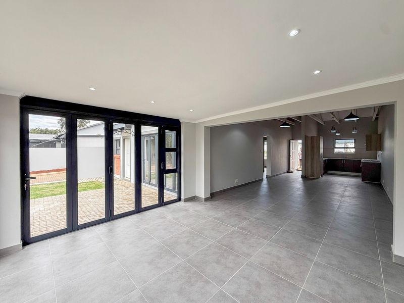 Spacious open-plan living and kitchen area featuring modern grey floor tiles, recessed lighting, and large bi-fold doors opening to an outdoor patio.