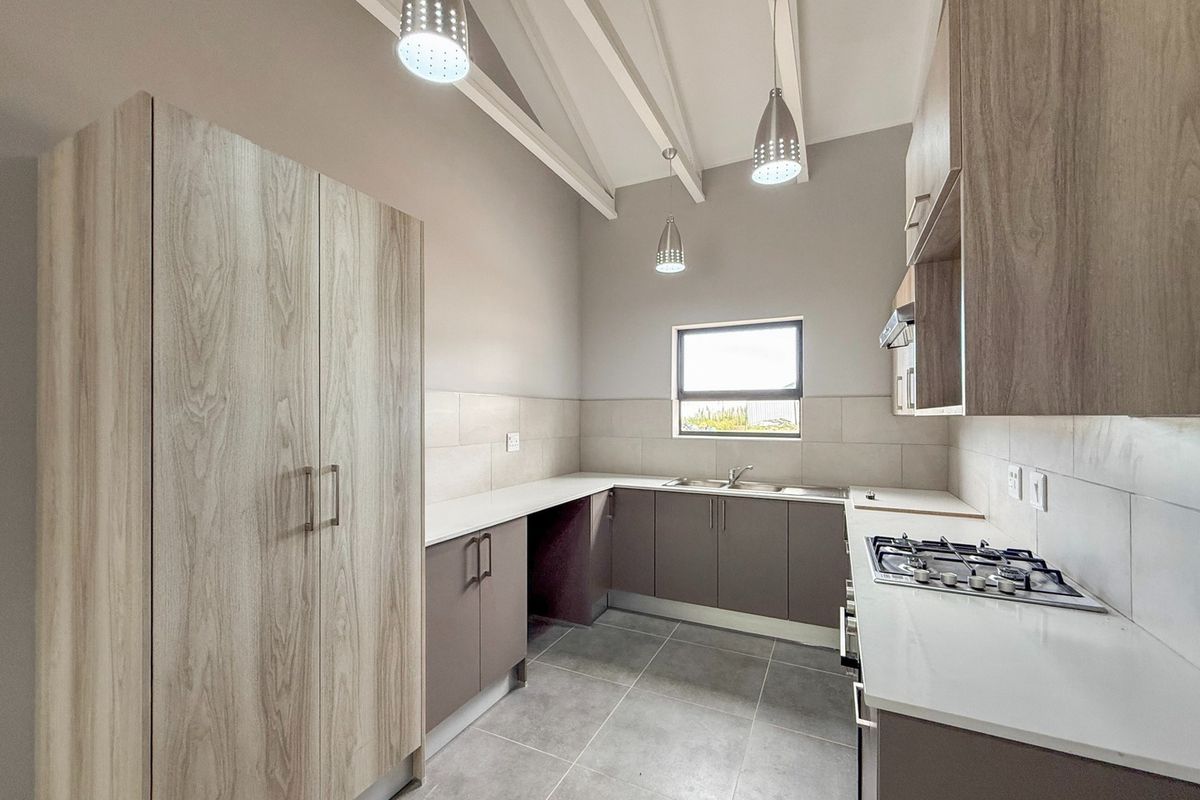 Modern kitchen featuring light wood-grain cabinetry, stone countertops, a gas hob, built-in oven, and high ceilings with exposed rafters.
