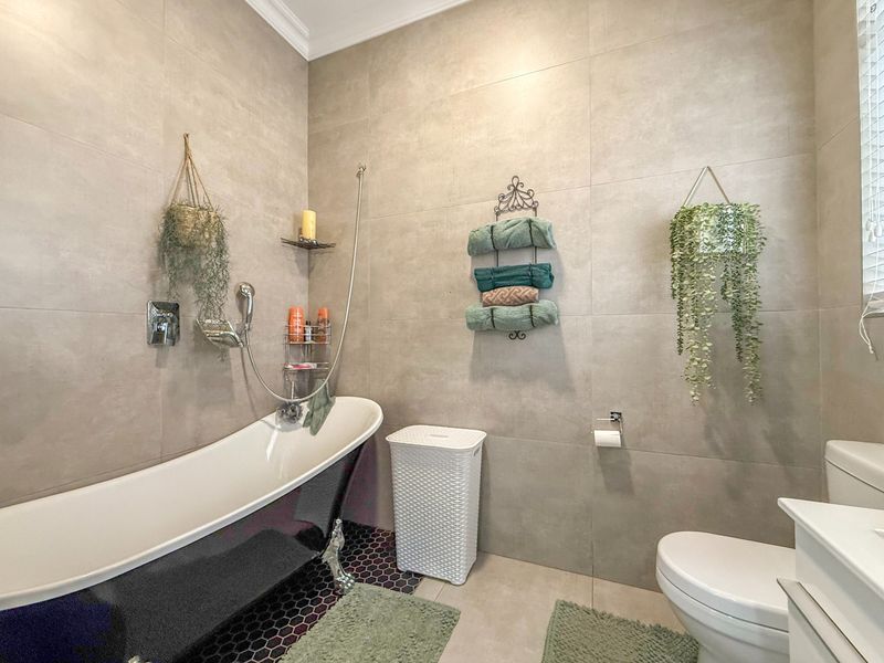 Modern bathroom featuring a sleek black freestanding bathtub, large format neutral wall tiles, hexagonal floor tiling, and a contemporary toilet and vanity setup.