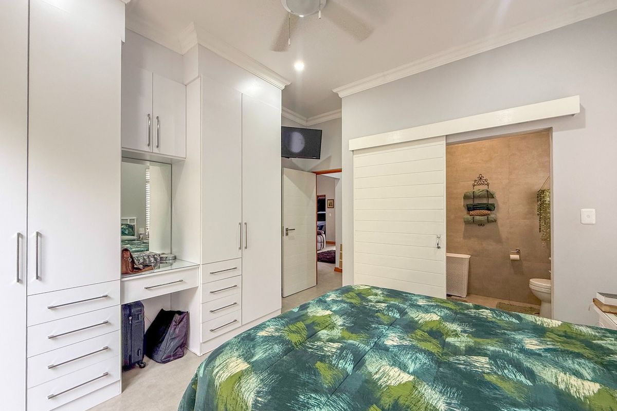 A well-maintained bedroom featuring extensive built-in cabinetry with a vanity, a ceiling fan, and a sliding barn door leading to an en-suite bathroom.