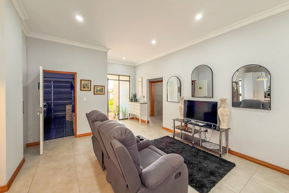 A well-maintained living room featuring neutral tiled flooring, recessed downlighting, and coved cornicing, with direct access to an outdoor area.