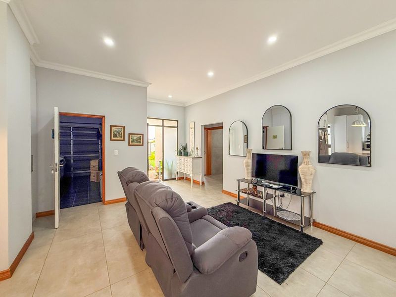 A well-maintained living room featuring neutral tiled flooring, recessed downlighting, and coved cornicing, with direct access to an outdoor area.