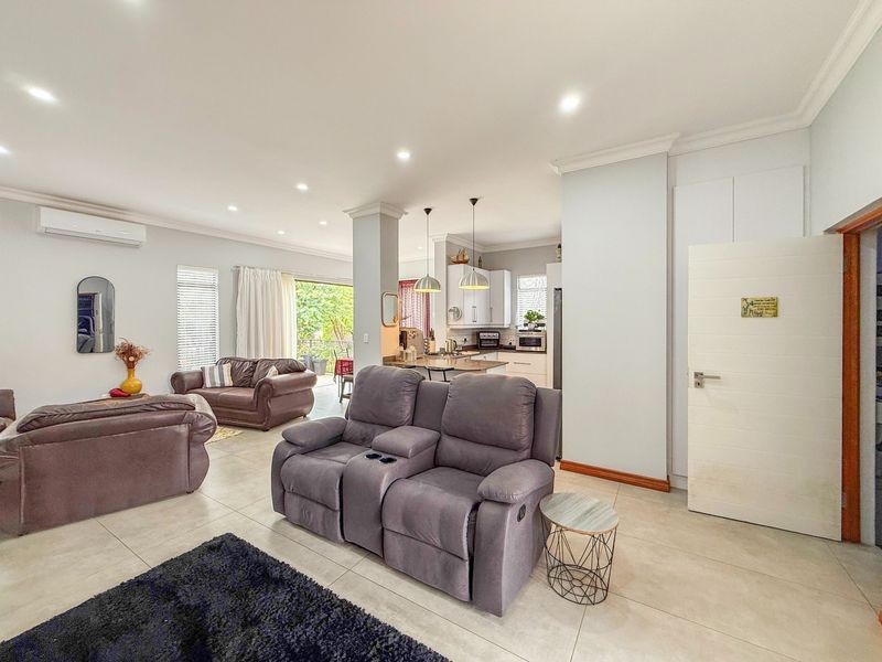 Spacious open-plan living area featuring tiled floors, recessed lighting, and a modern kitchen with an island, seamlessly connecting to the outdoor patio.