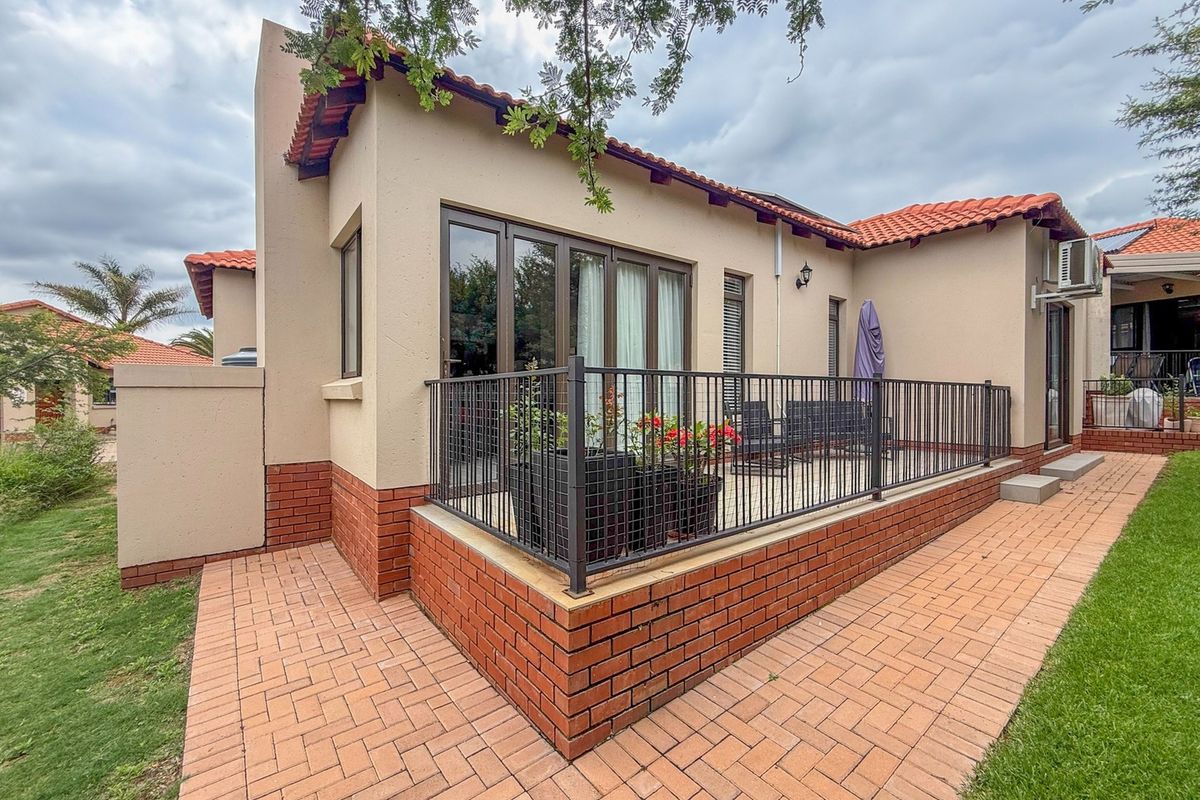 Rear view of the property featuring a paved patio area, brick base detailing, terracotta roof tiles, and secure metal railing.