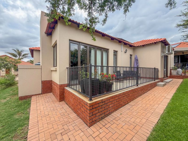 Rear view of the property featuring a paved patio area, brick base detailing, terracotta roof tiles, and secure metal railing.