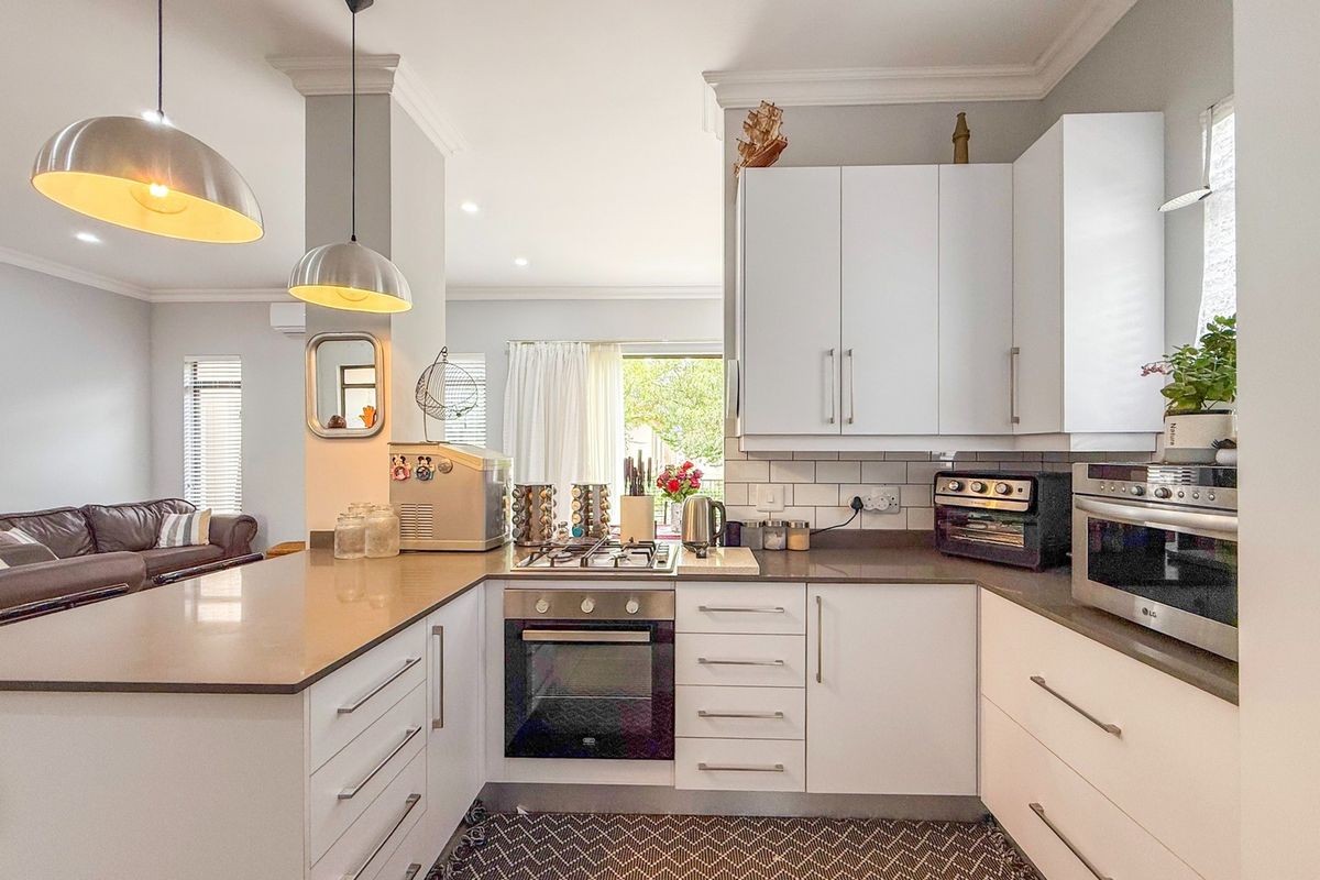 Modern kitchen featuring white cabinetry, stone countertops, subway tile backsplash, and integrated stainless steel oven and gas hob, flowing into the living area.