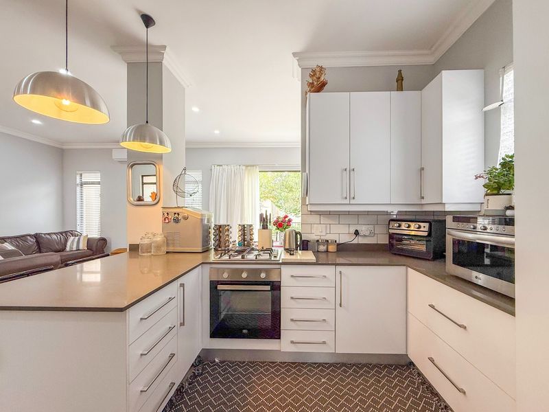 Modern kitchen featuring white cabinetry, stone countertops, subway tile backsplash, and integrated stainless steel oven and gas hob, flowing into the living area.
