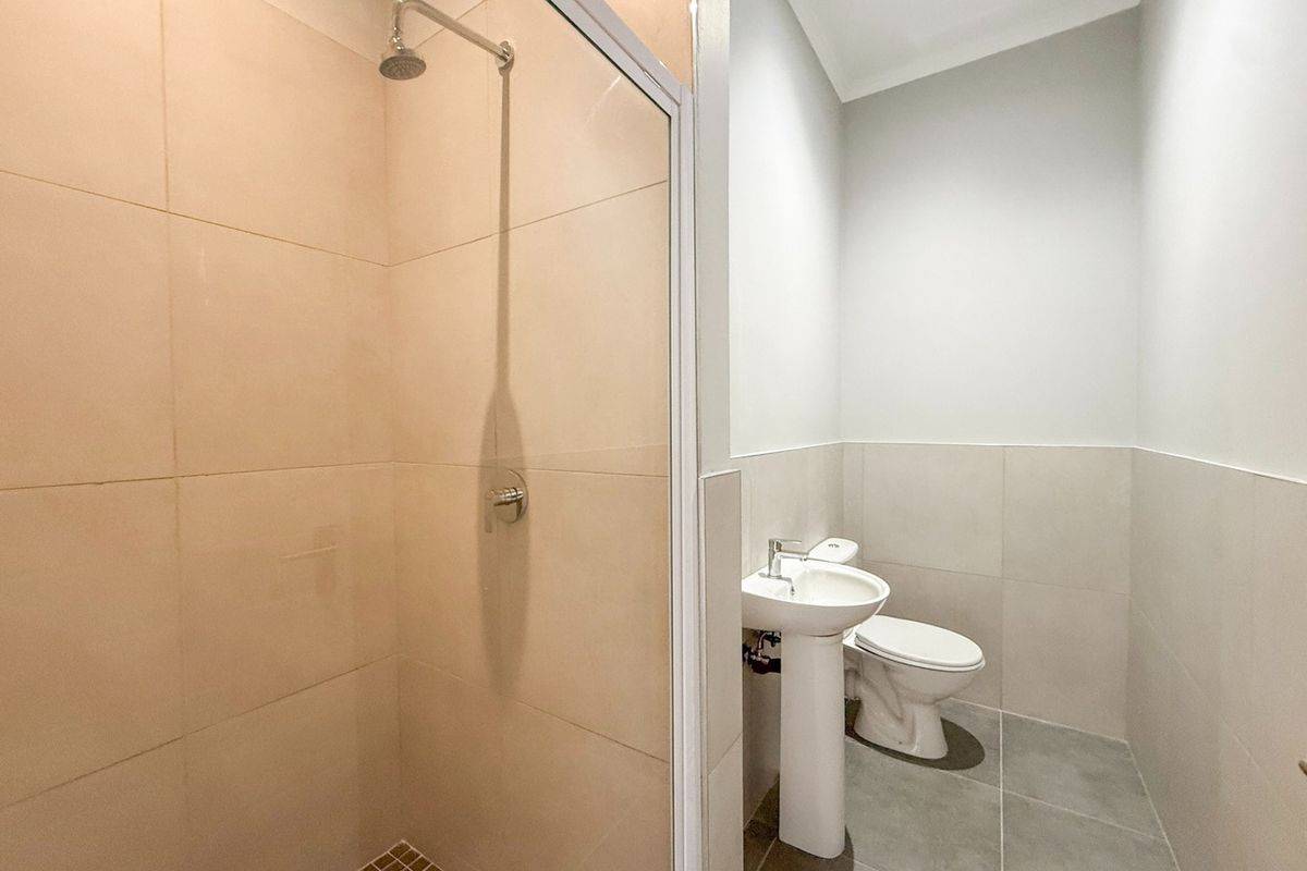 A clean, modern bathroom featuring a glass-enclosed shower, pedestal basin, and toilet with neutral wall and floor tiling.