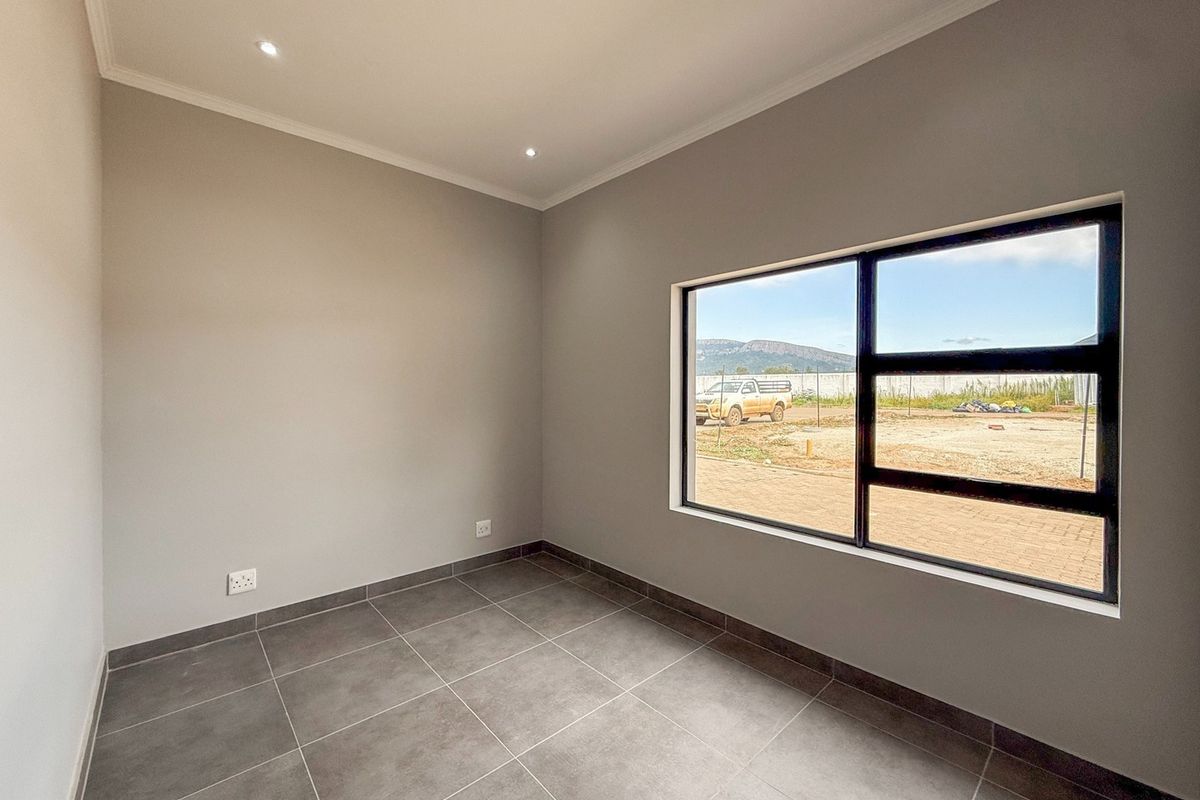 A bright, empty bedroom featuring modern grey floor tiles, recessed downlighting, and a large window with views of the surrounding estate.