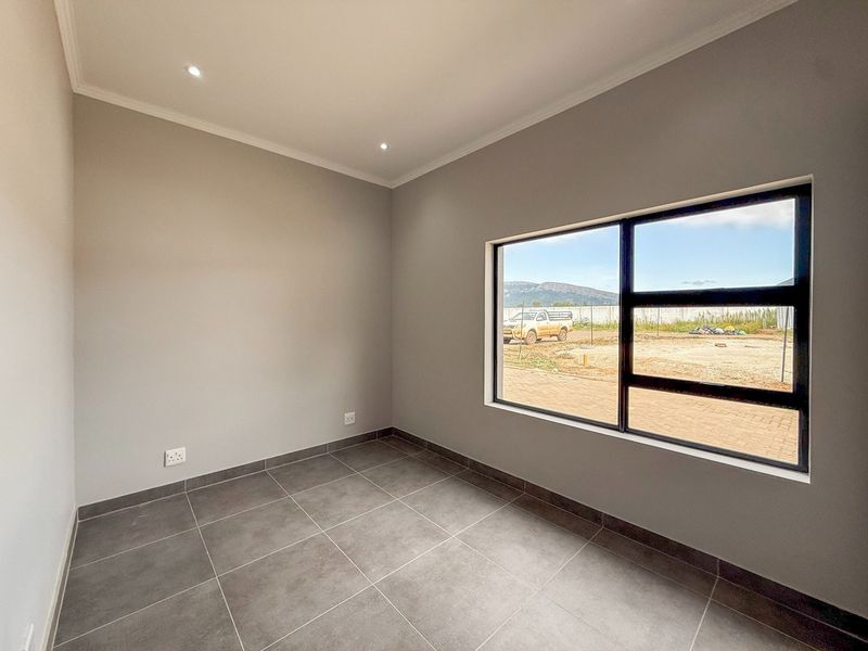 A bright, empty bedroom featuring modern grey floor tiles, recessed downlighting, and a large window with views of the surrounding estate.
