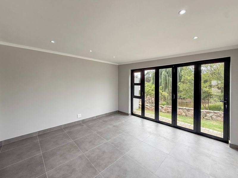 A bright, modern living area featuring large black aluminium stacker doors that open to a garden view, complemented by neutral tiled flooring and recessed lighting.