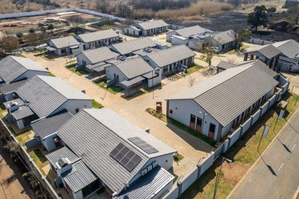 Aerial view of a modern retirement village complex featuring multiple residential units with tiled roofs, solar panels, and paved access roads.