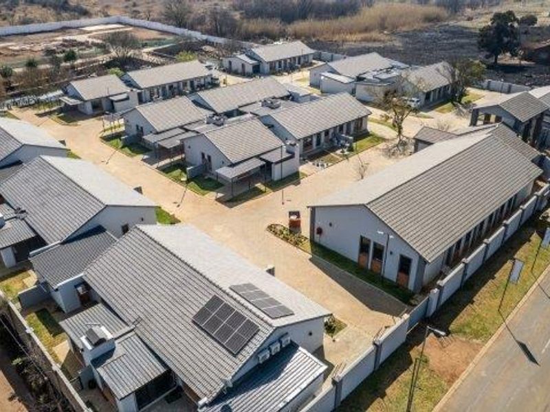 Aerial view of a modern retirement village complex featuring multiple residential units with tiled roofs, solar panels, and paved access roads.