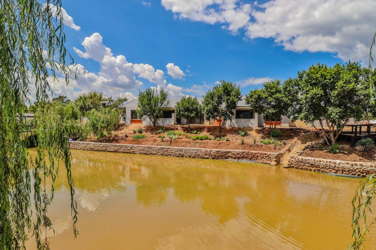 A scenic rear view of the retirement village property featuring a landscaped garden, stone retaining wall, and a tranquil pond.