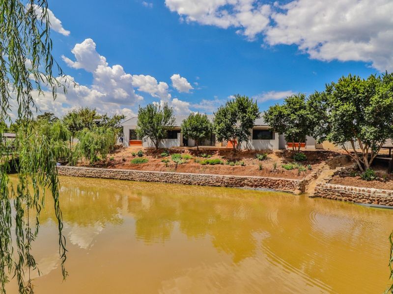 A scenic rear view of the retirement village property featuring a landscaped garden, stone retaining wall, and a tranquil pond.