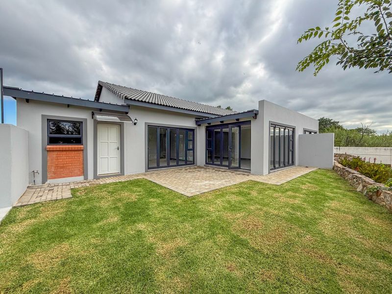 Rear view of the property featuring a paved patio area, modern bi-fold doors, and a well-maintained garden with a stone retaining wall.